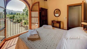 A bedroom with a bed, a wooden wardrobe, a bedside table, a mirror, and a balcony with a view of the countryside. - Trebbiano-Panoramic apartment with swimming pool and vineyard (Reggello)