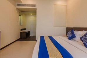 A hotel room with a bed, a bedside table, a mirror, and a door leading to a bathroom. - Hotel Aura (Mumbai)