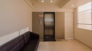 A modern hotel lobby with a black leather sofa, a reception desk, and a glass elevator. - Hotel Aura (Mumbai)