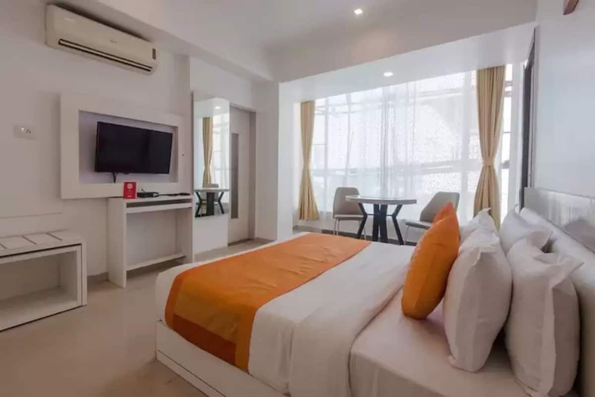 Quarto de hotel com cama, escrivaninha, televisão e janela com cortinas.