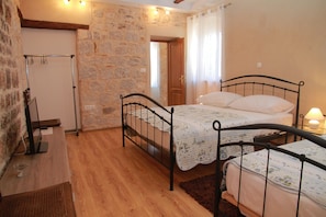 A bedroom with two beds, a stone wall, wooden flooring, and a small desk with a lamp. - Dolce Vita Apartments (Split)
