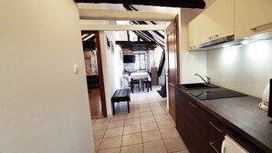 Una cocina con microondas integrado, un lavamanos y armarios de madera. Se ve un comedor con mesa y sillas al fondo.