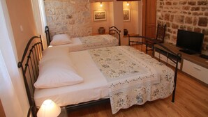 Un dormitorio con dos camas, un escritorio de madera, una televisión y paredes de piedra.