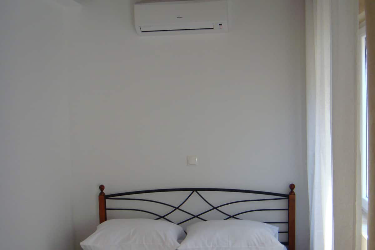 Un lit simple avec une tête de lit en bois et une couvre-lit marron, dans une pièce aux murs blancs et aux poutres apparentes.