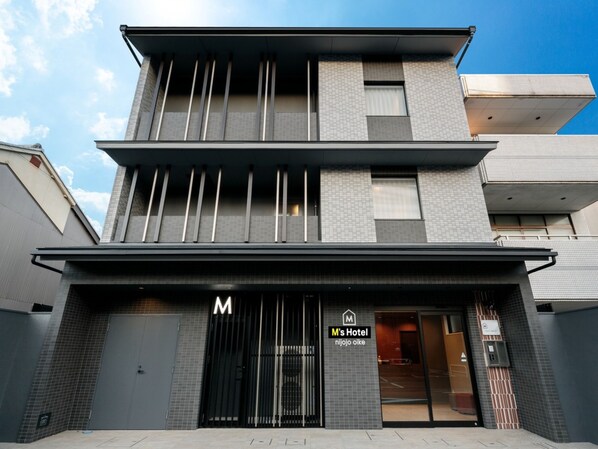 A modern hotel with a prominent 'M's Hotel' sign, a gated entrance, and a visible parking area. - M’s Hotel Nijojo Oike (Kyoto)