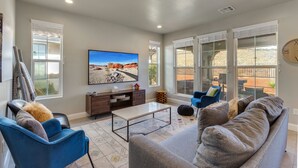 Un salón amplio con un televisor de pantalla plana grande, asientos cómodos y ventanas grandes que ofrecen vistas al exterior.