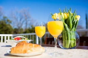 A table with a croissant, two glasses of orange juice, a bowl of strawberries, and a vase of tulips.