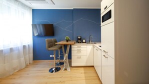 Eine kompakte Küche mit blauer Akzentwand, einem Wand-Fernseher und einer kleinen Essecke.