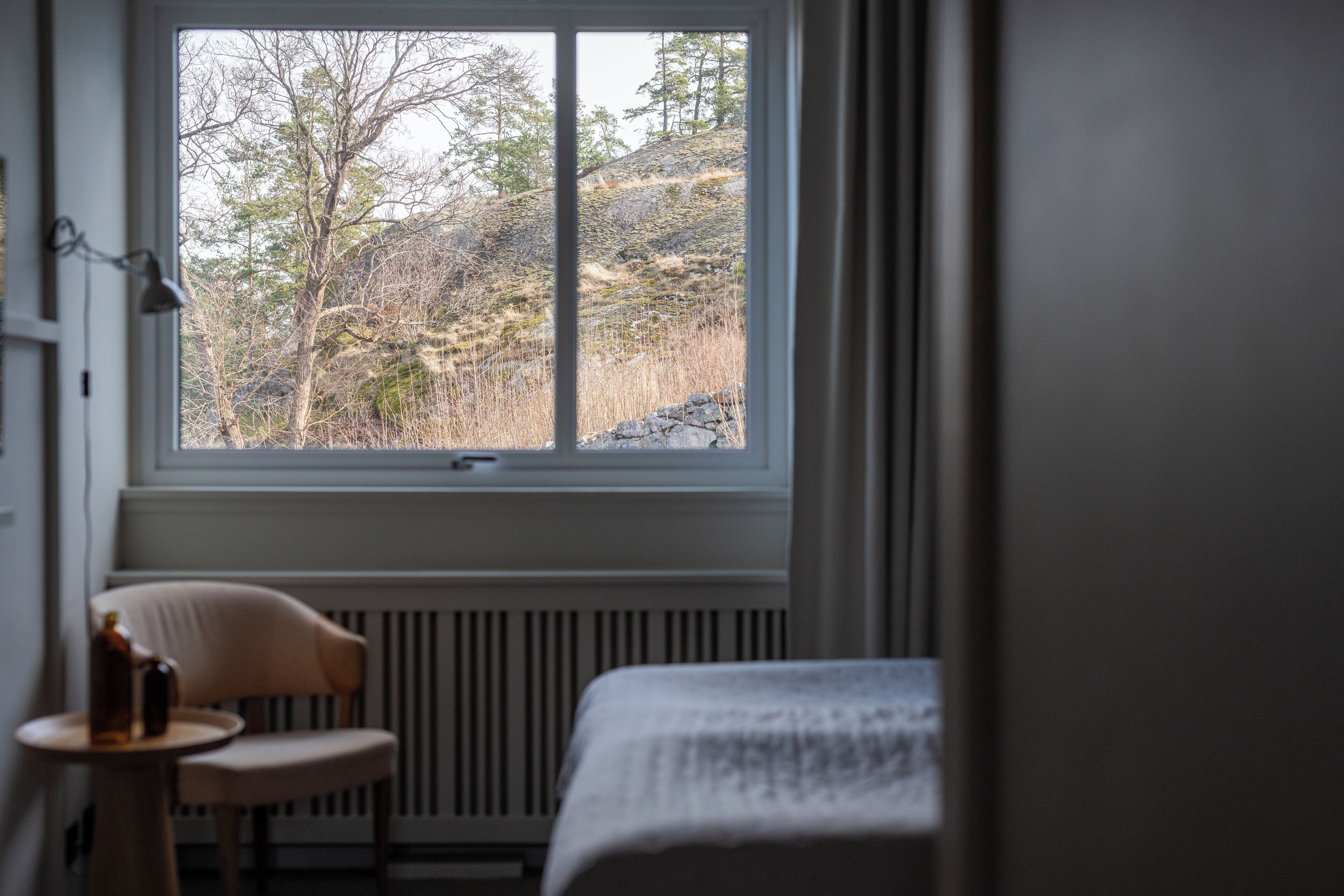 A room with a bed, a chair, and a window overlooking a hillside.