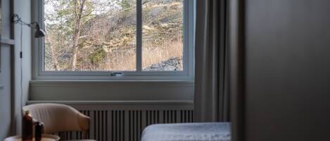 A room with a bed, a chair, and a window overlooking a hillside.