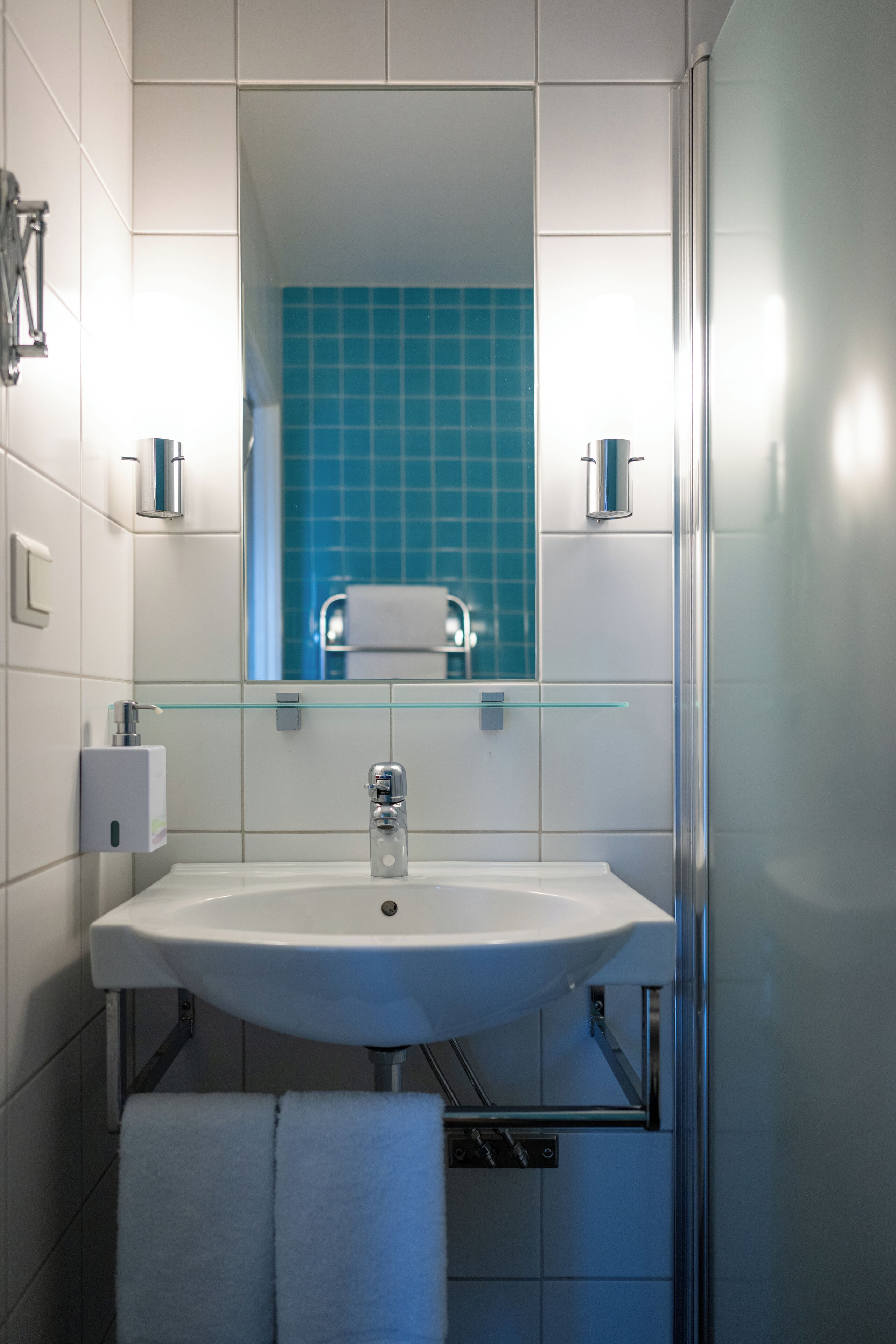 A bathroom with a white sink, a glass shelf, a towel rack, and a mirror.