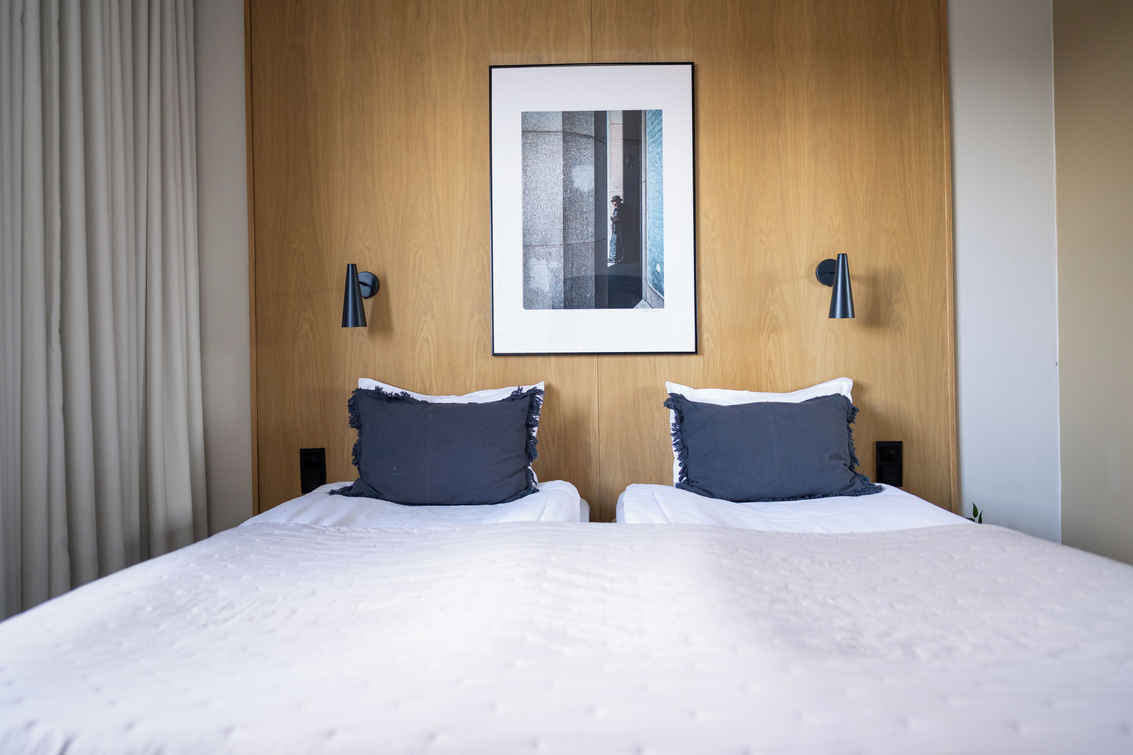 A hotel room with a large bed, two bedside tables, a framed picture on the wall, and a curtain on the left.