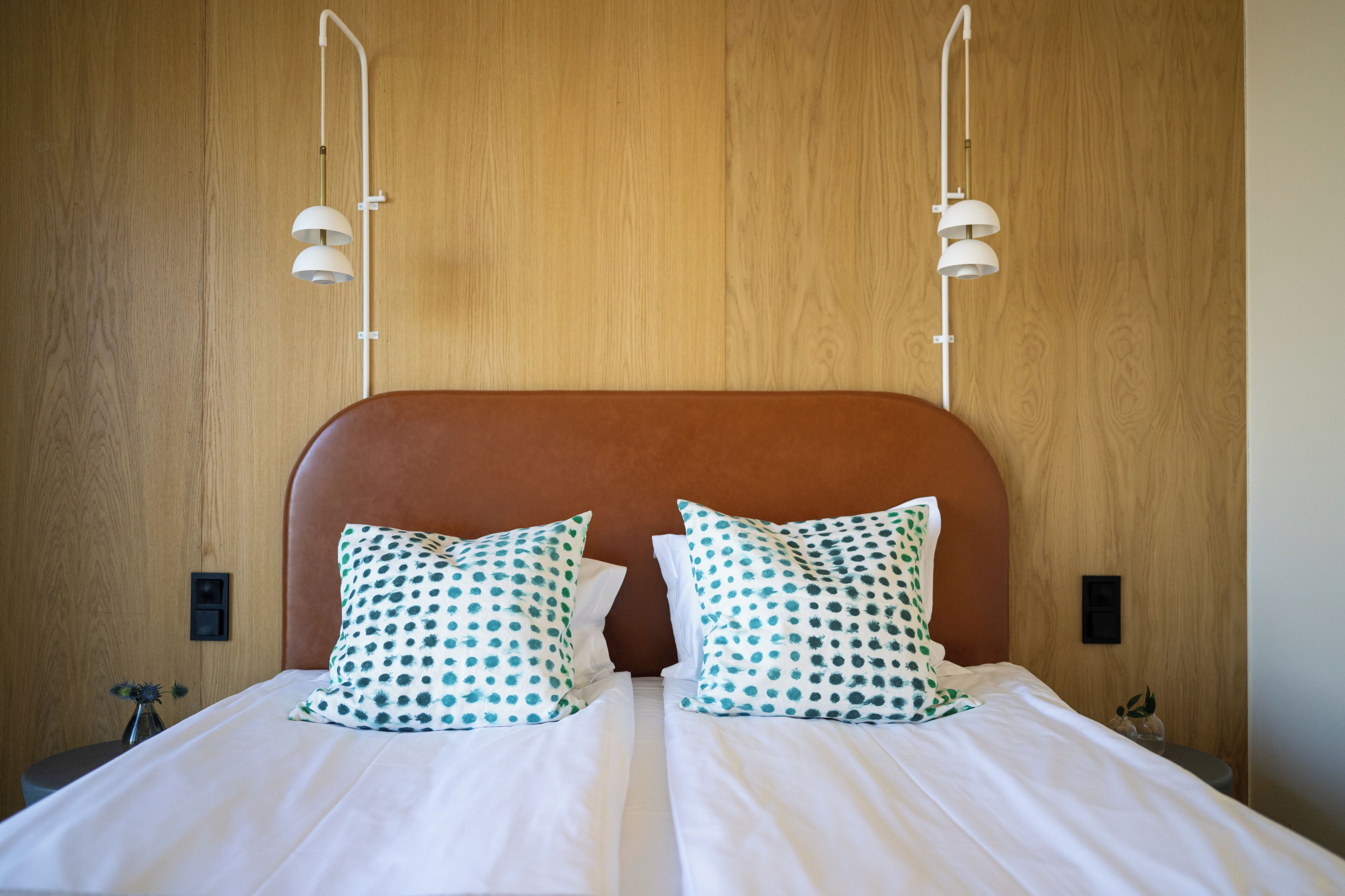 A double bed with white bedding and teal polka dot pillows, two bedside tables, and a wooden headboard.
