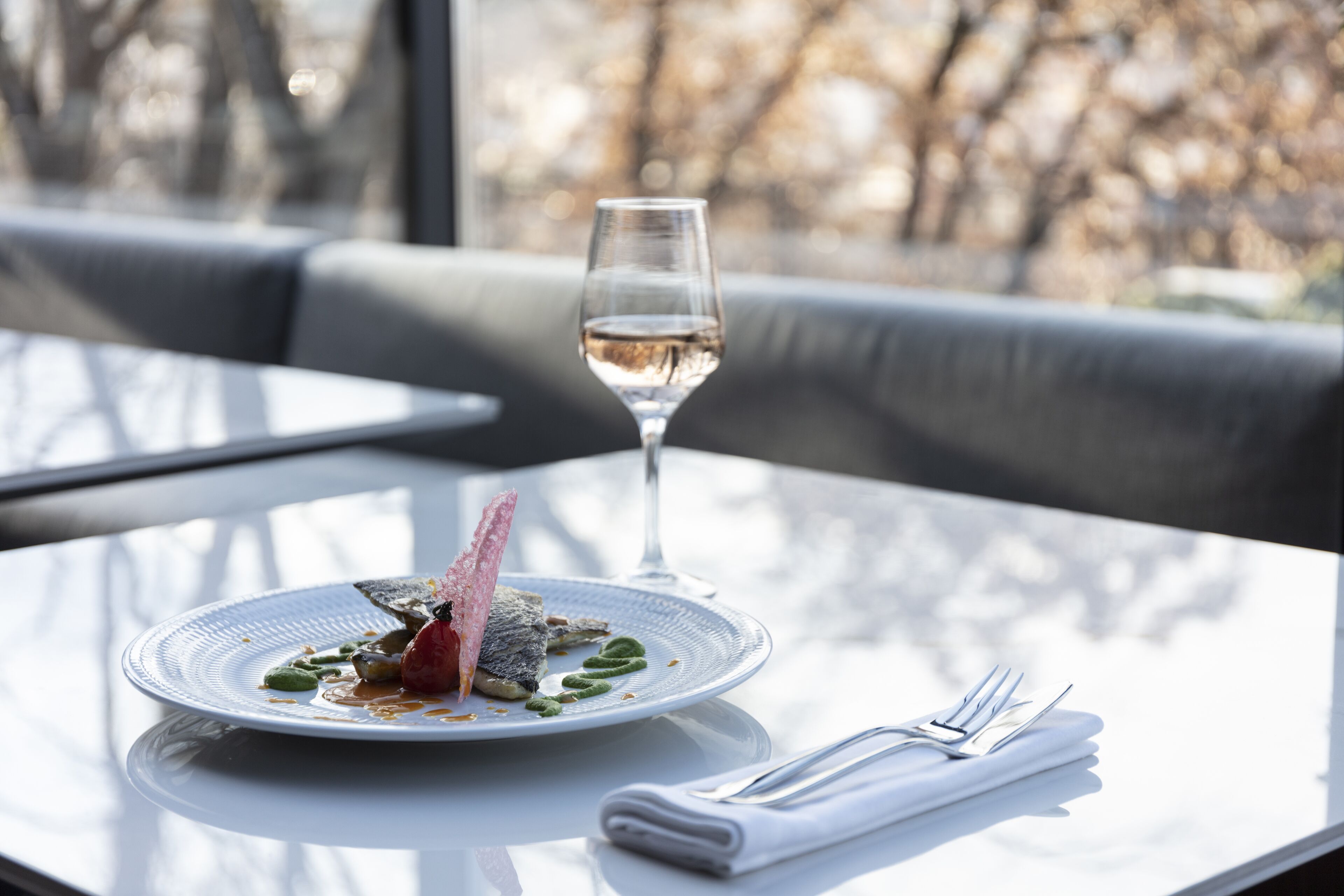 Ein Esstisch mit einem Teller Essen, einem Glas Weißwein und einem gefalteten Servietttuch.