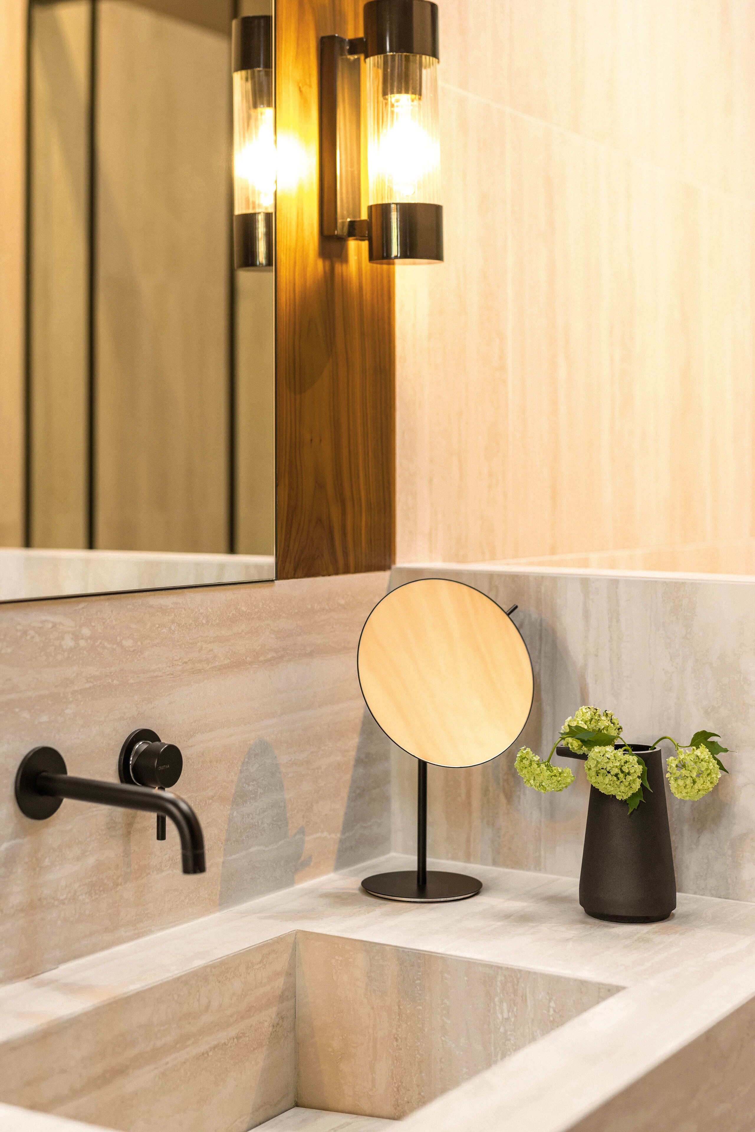 Een badkamer met een moderne wastafel, een ronde spiegel en een wandlamp.