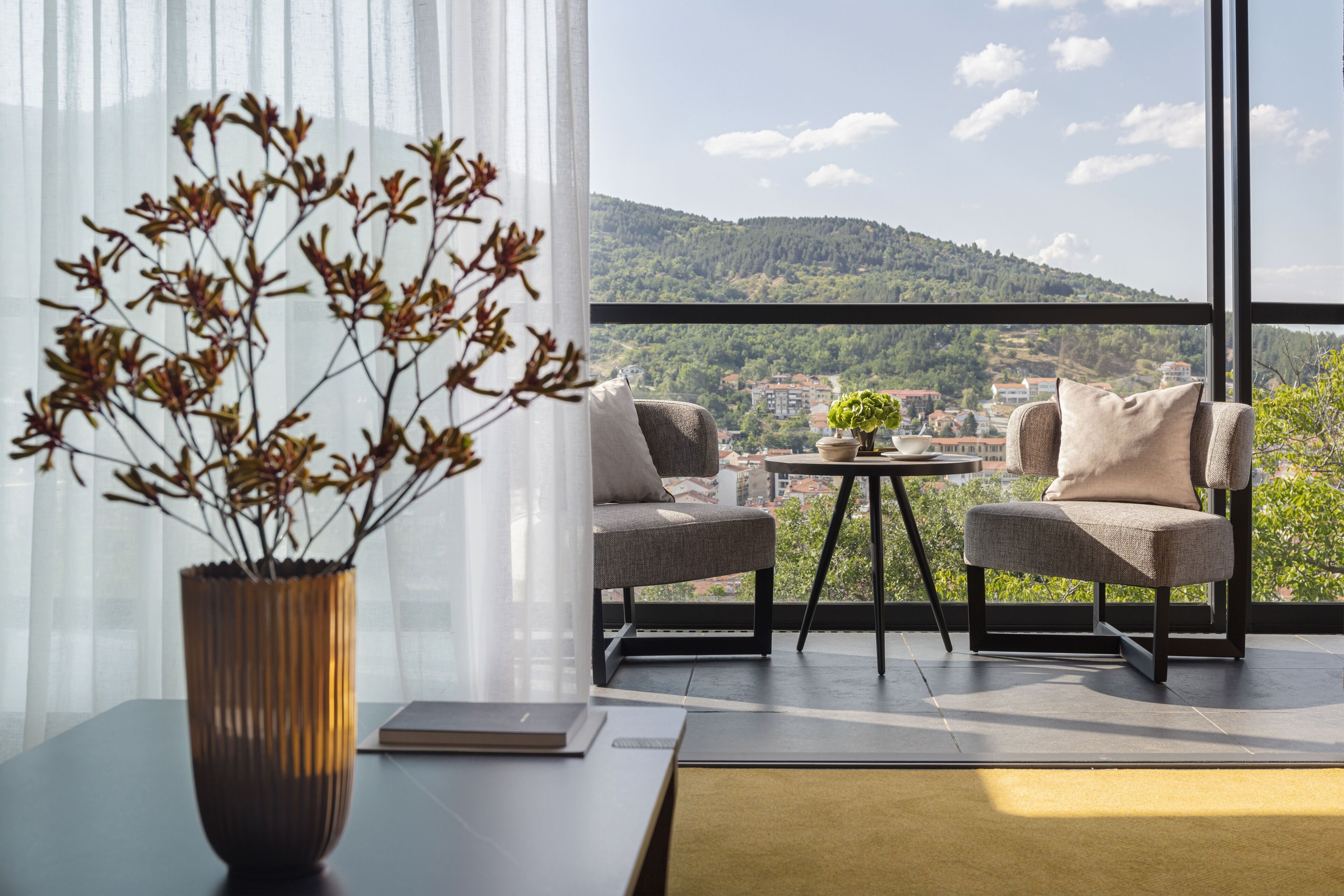 Ein Balkon mit zwei Stühlen, einem kleinen Tisch und einer Vase mit getrockneten Zweigen.