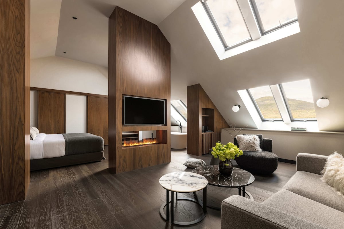 A modern loft bedroom with a large TV, a fireplace, and skylights.