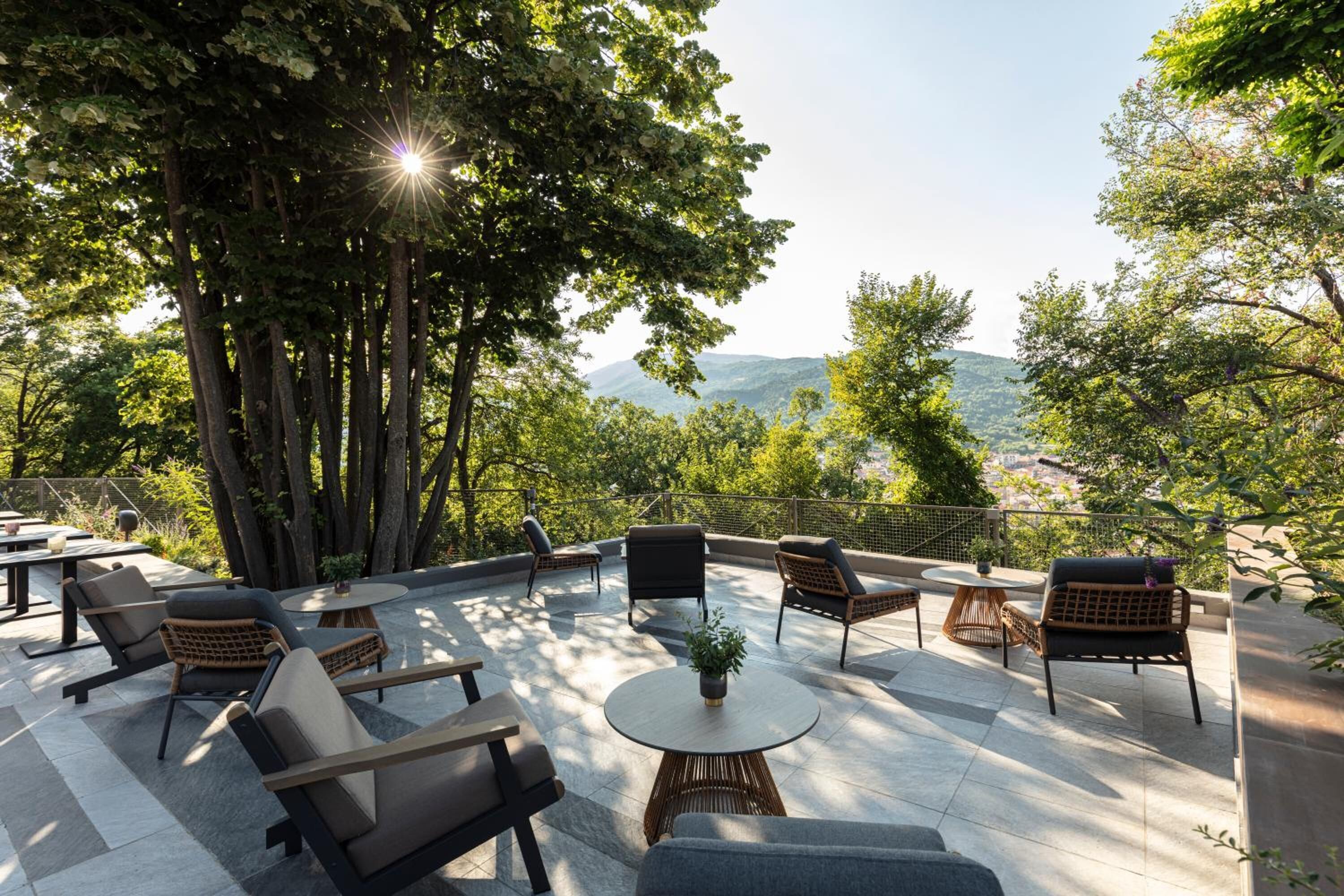 Un espacio al aire libre con varias sillas y mesas, rodeado de árboles y vistas a colinas distantes.