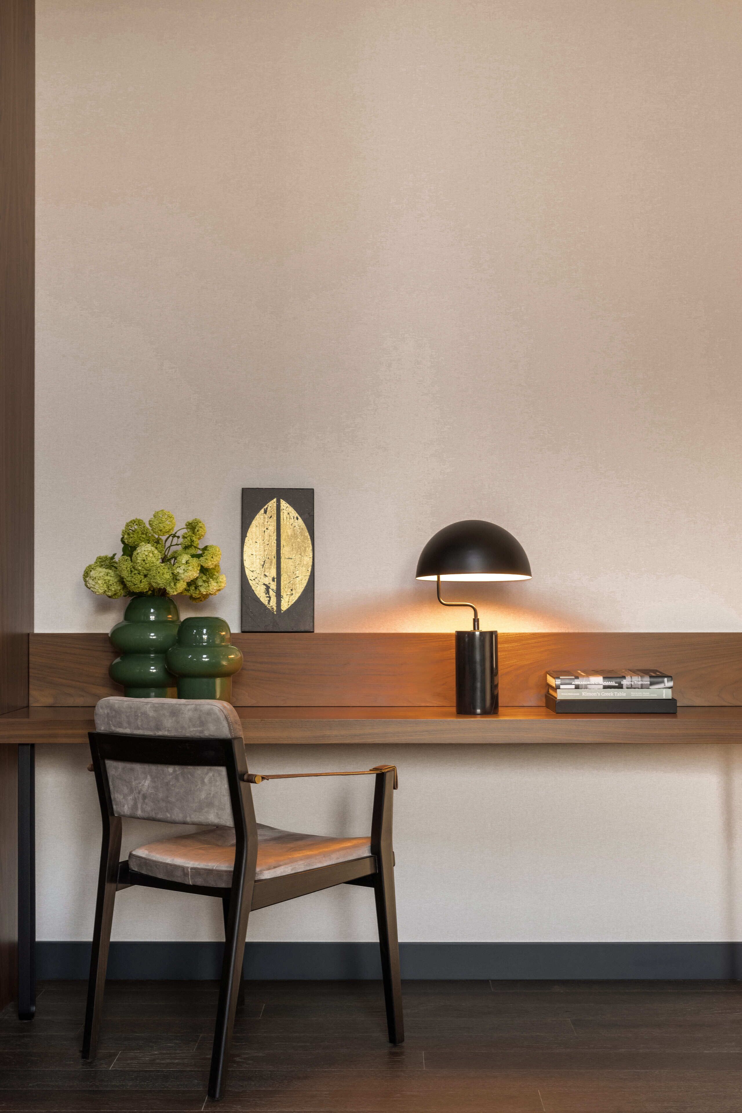 A modern desk with a lamp, a chair, and a vase of flowers.