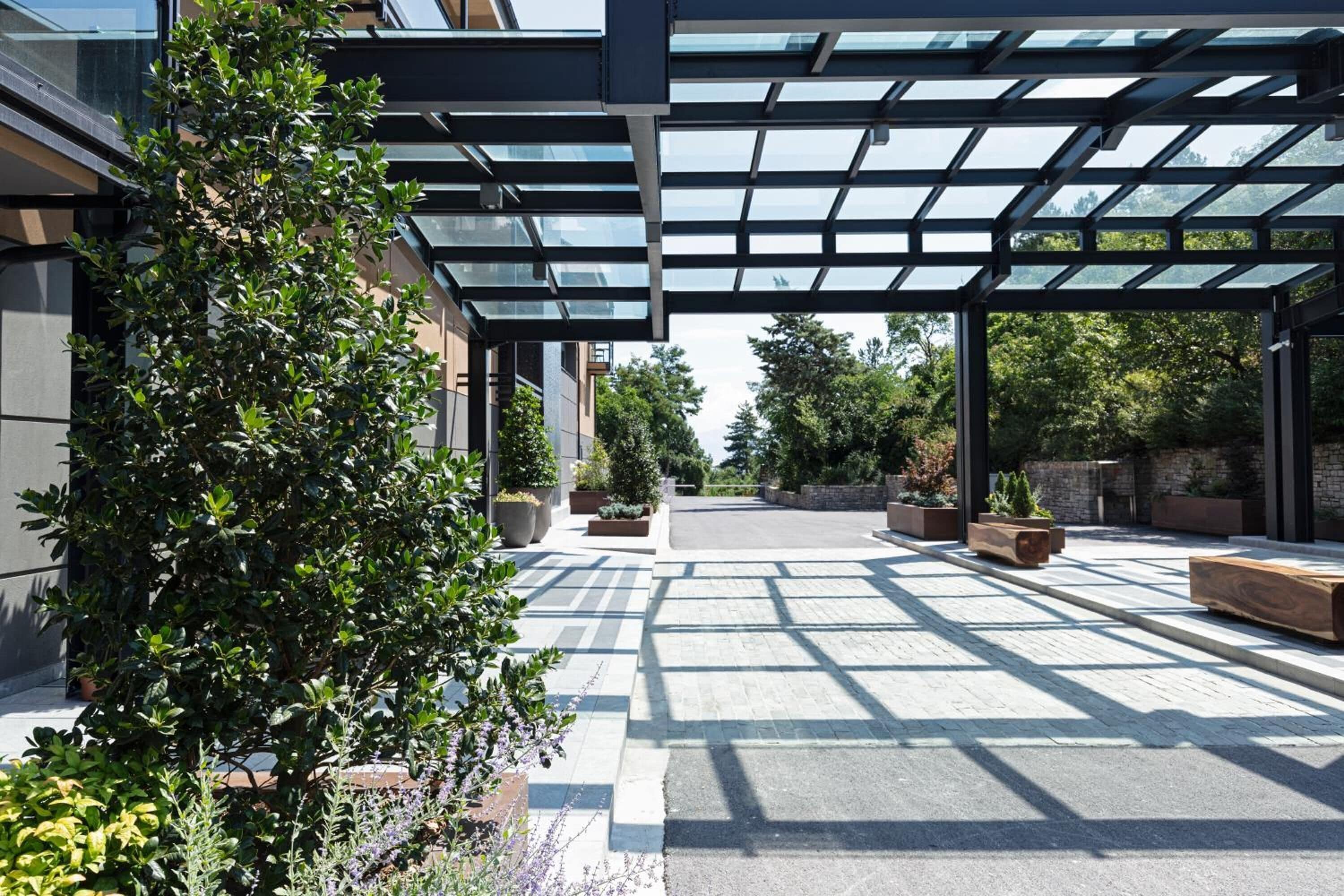 A covered outdoor area with a glass roof, potted plants, and a paved walkway.