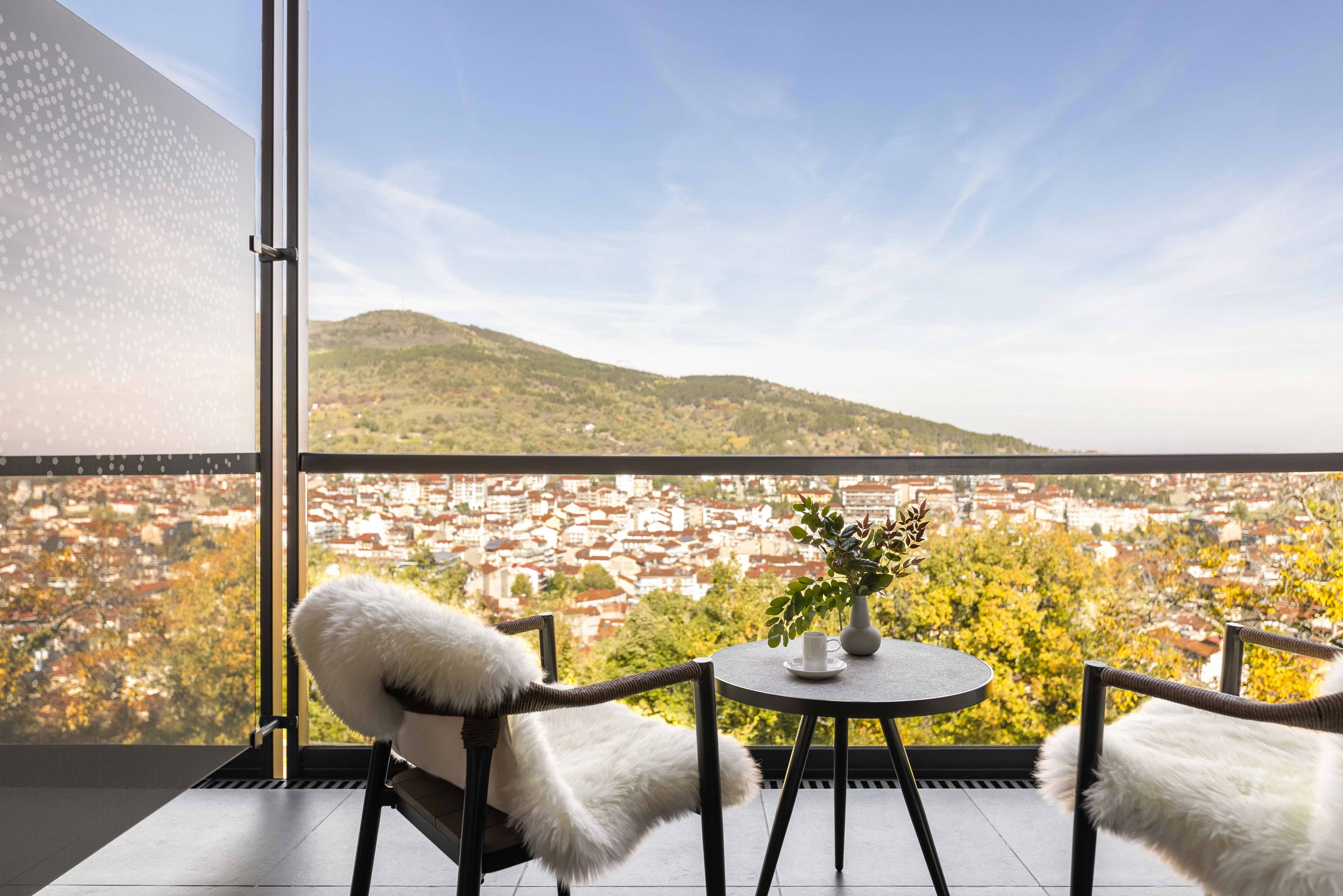 Een balkon met twee stoelen, een tafeltje en een vaas met een plant.