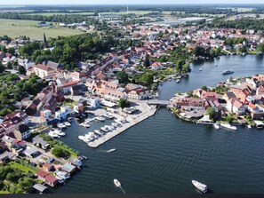 Vista aérea de un pueblo a orillas del río, con edificios históricos, un puente y un puerto deportivo con barcos.