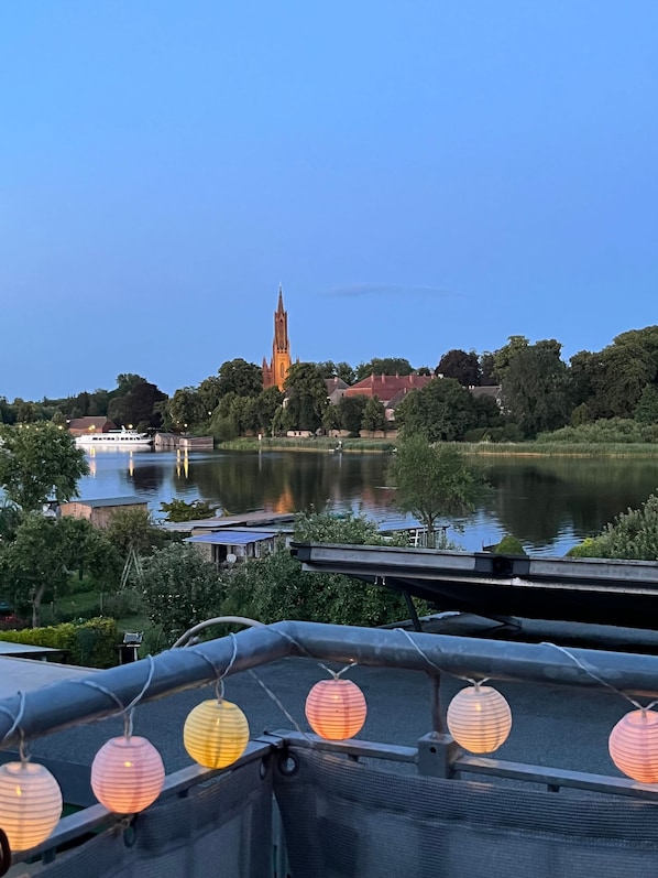 Une vue sur la rivière, avec le clocher d’une église, des arbres et un pont.