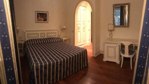Une chambre à coucher comprenant un lit, un bureau, une chaise, une lampe et une porte donnant sur une autre pièce.