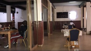 Un comedor con mesas y sillas, un separador de madera y una lámpara fijada a la pared.