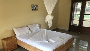 Una cama de madera con ropa de cama blanca, una mesita de noche de madera y una mosquitera.