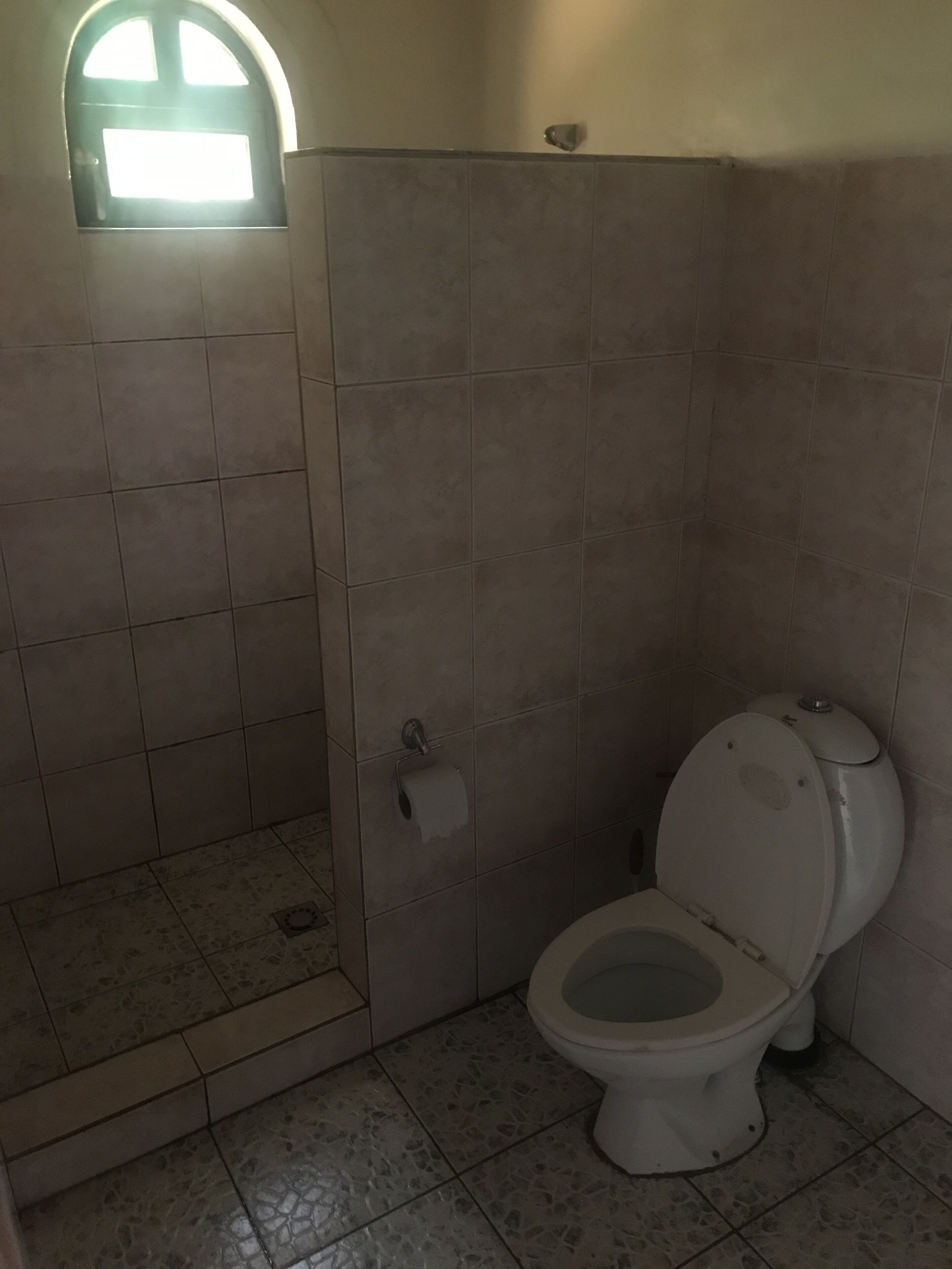 Un baño con inodoro, cabina de ducha y un ventanal.
