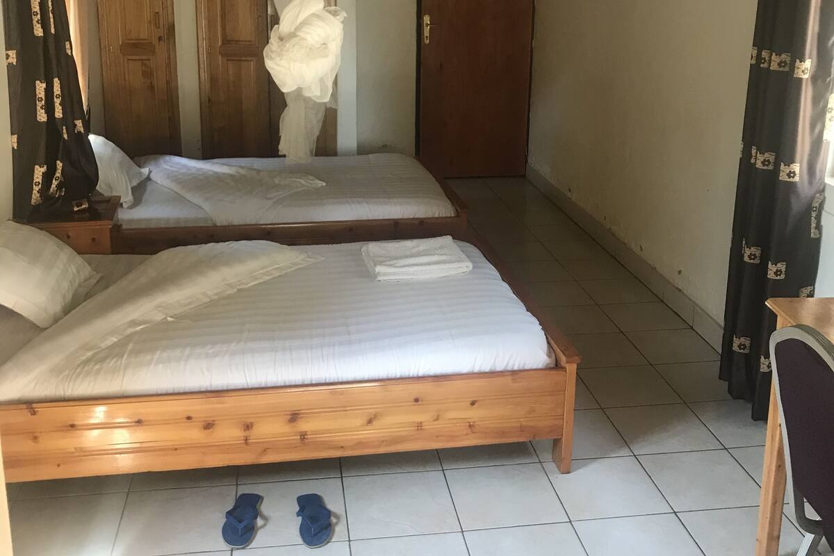 Une pièce avec deux lits en bois, une chaise en bois, une porte et un rideau.