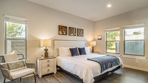 A bedroom with a bed, nightstands, a chair, and artwork on the wall.
