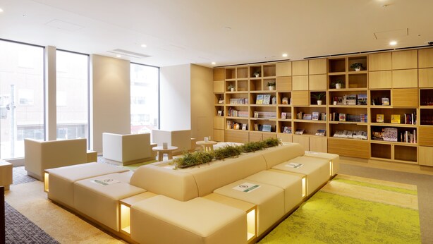 A modern library with a long sofa, bookshelves, and a bright window view. - JR Inn Sapporo Kita 2jo (Sapporo)