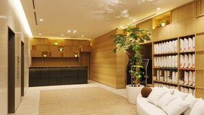 A modern hotel lobby with a reception desk, a seating area with a sofa, and a storage unit with pillows. - JR Inn Sapporo Kita 2jo (Sapporo)