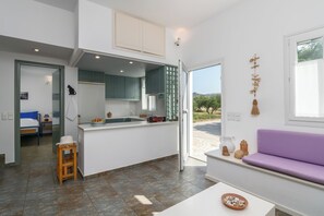 A modern kitchen with a central island, a dining area with a purple sofa, and a view of the outdoors. - Villa in an oasis of peace close to the most beautiful beaches and all Milos services (Milos)