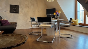 A modern loft with a dining area featuring a table and chairs, a television, and a chandelier. - Gästehaus Susanne Pfaffmann (Landau in der Pfalz)