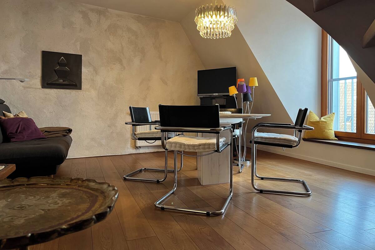 A modern loft with a dining area featuring a table and chairs, a television, and a chandelier.