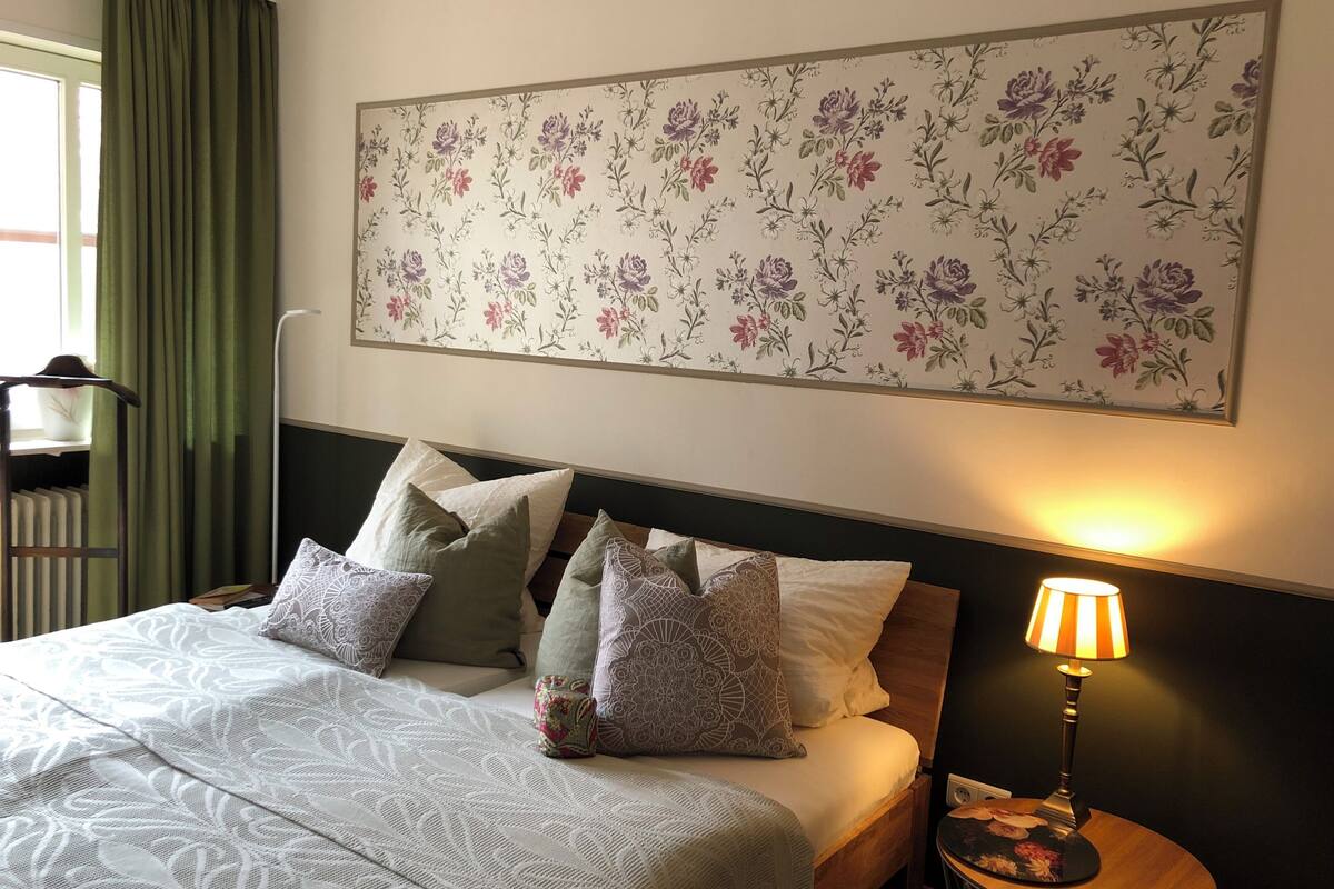 A neatly made bed with patterned pillows, a floral wall art piece, and a bedside lamp.