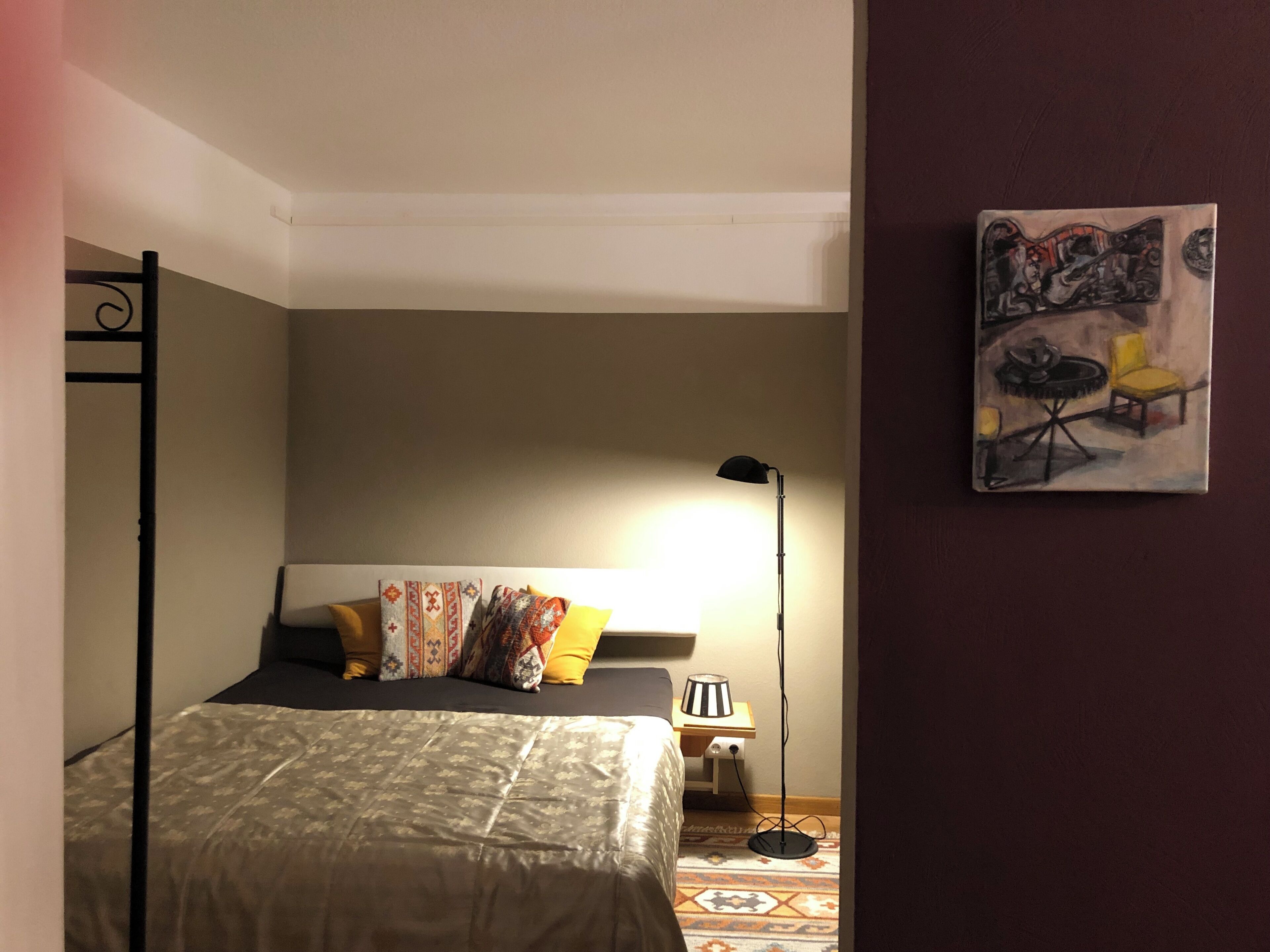 A bedroom with a bed, a bedside table, a lamp, and a wall-mounted artwork.