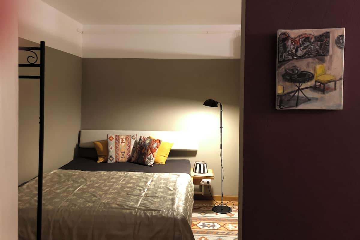 Ein Schlafzimmer mit einem Bett, einem Nachttisch, einer Lampe und einem Wandbild.