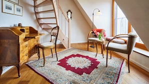 A room with a wooden desk, two chairs, a patterned rug, a staircase, and a window with a view. - Gästehaus Susanne Pfaffmann (Landau in der Pfalz)