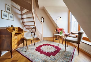 A room with a wooden desk, two chairs, a patterned rug, a staircase, and a window with a view. - Gästehaus Susanne Pfaffmann (Landau in der Pfalz)