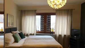 A hotel room with a bed, a television, a window with curtains, and a chandelier. - Gästehaus Susanne Pfaffmann (Landau in der Pfalz)