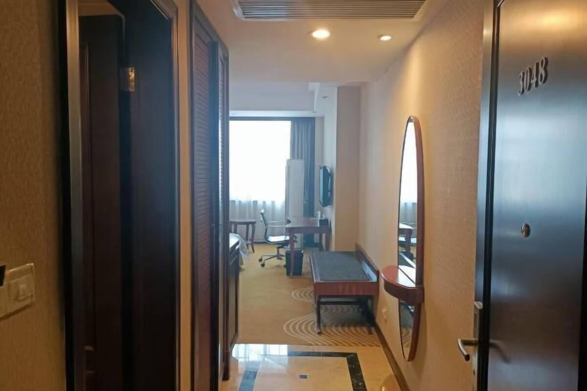 Corredor de hotel com uma porta identificada como '3048', uma mesa, uma cadeira e uma televisão.