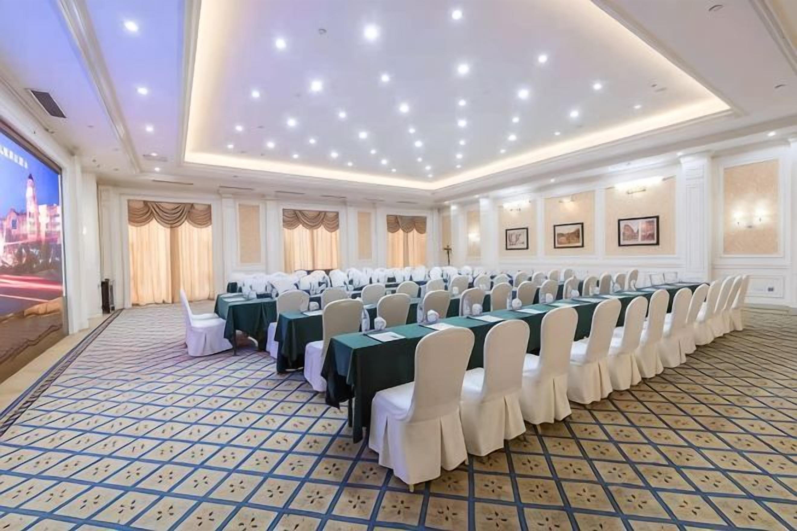 A conference room with a long table, white chairs, and a patterned carpet.
