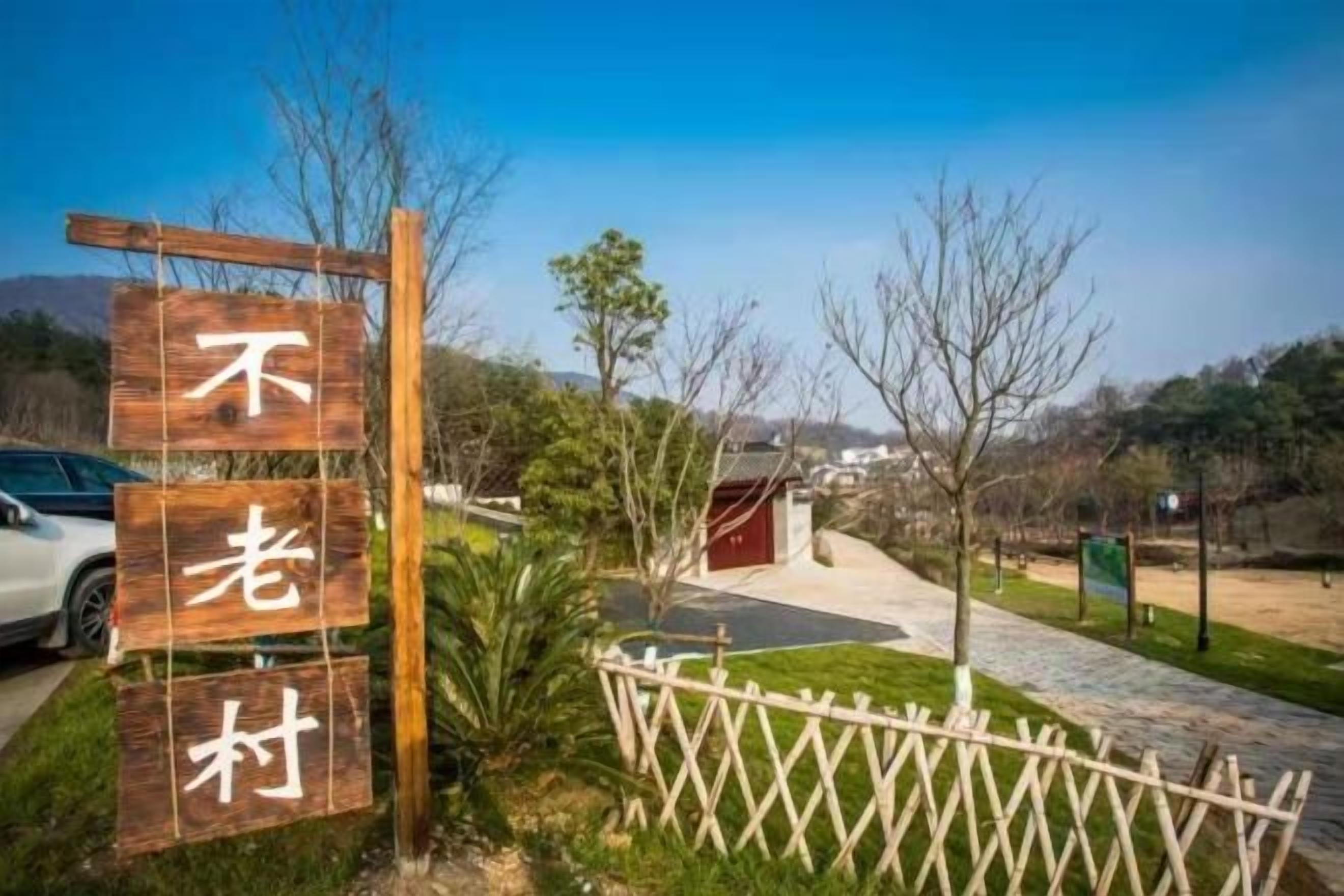 A wooden sign with Chinese characters, a fenced area, and a pathway leading to a building.