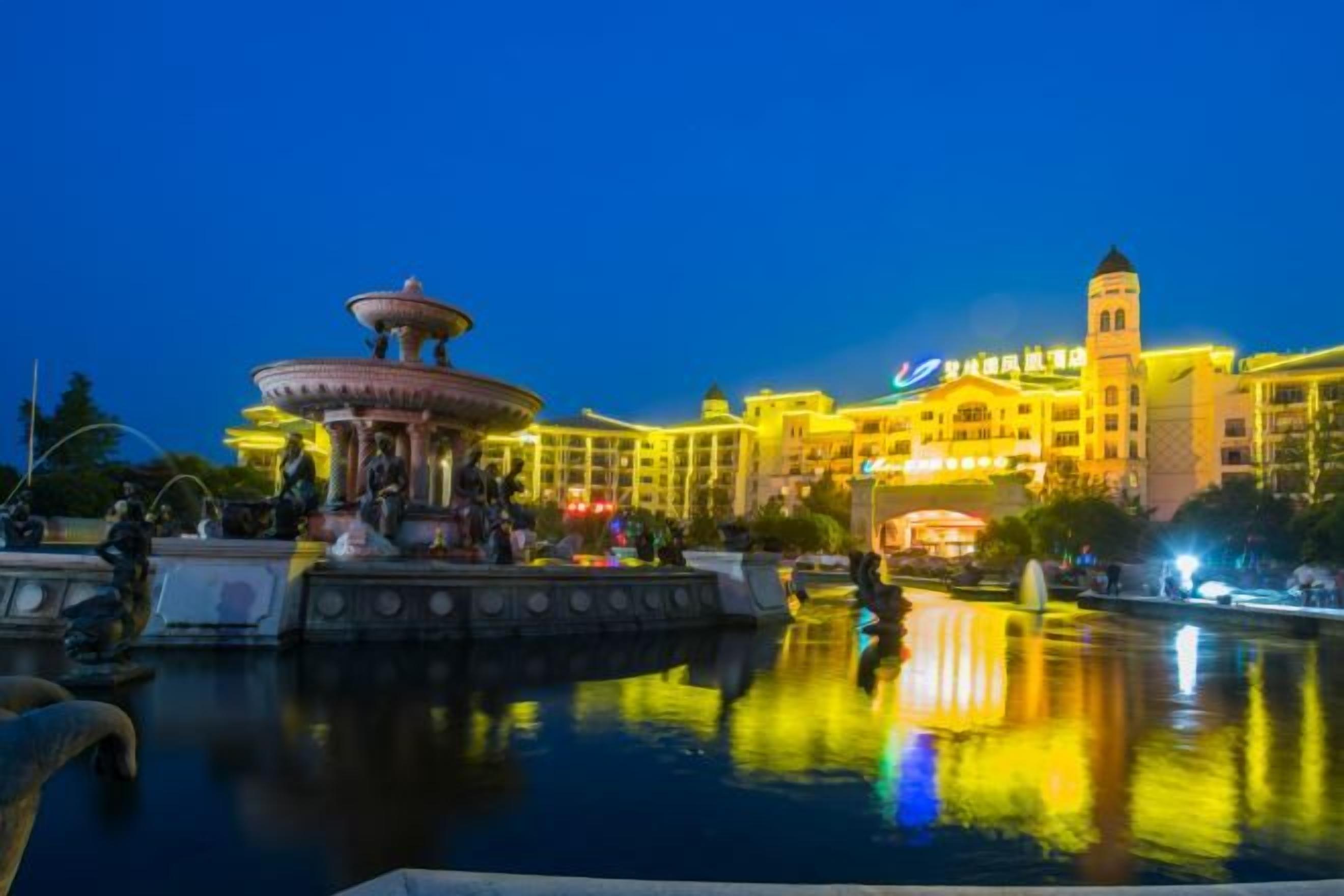 A nighttime view of a hotel with a fountain in the foreground and a building with illuminated signage in the background.