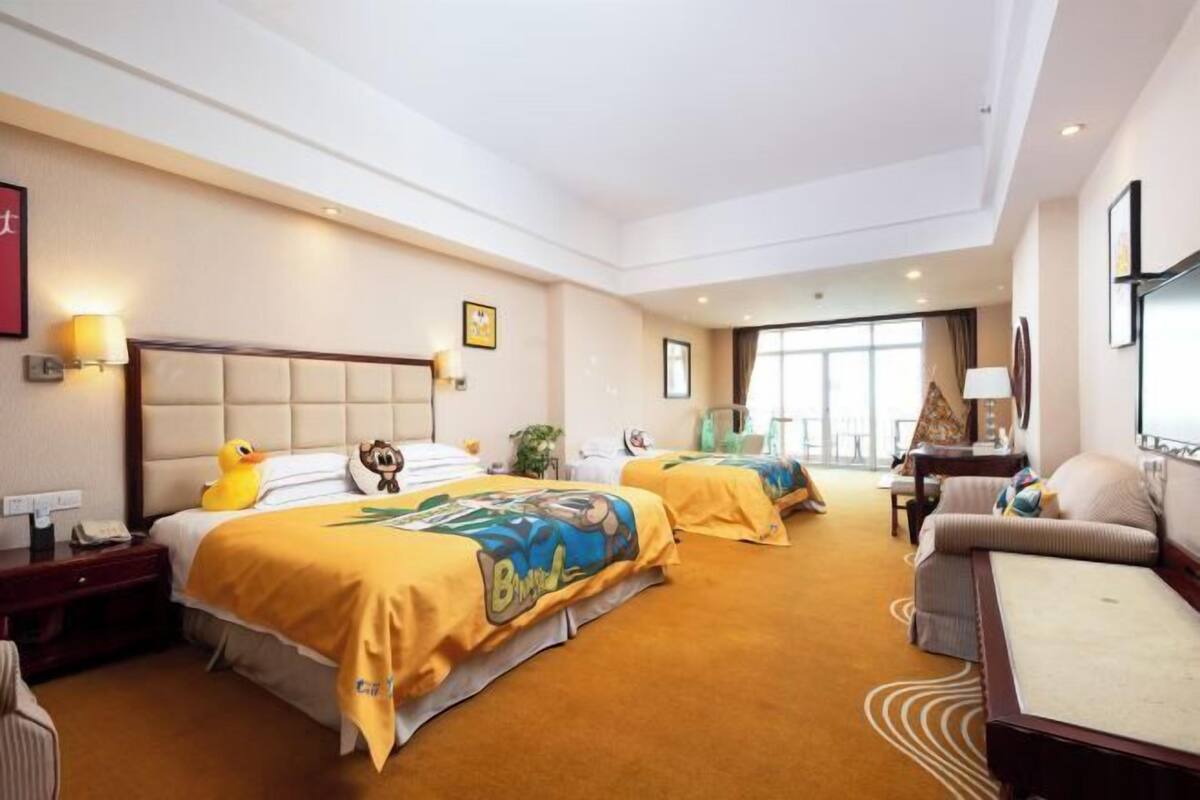 Quarto de hotel com duas camas, um sofá, uma escrivaninha e uma janela grande.