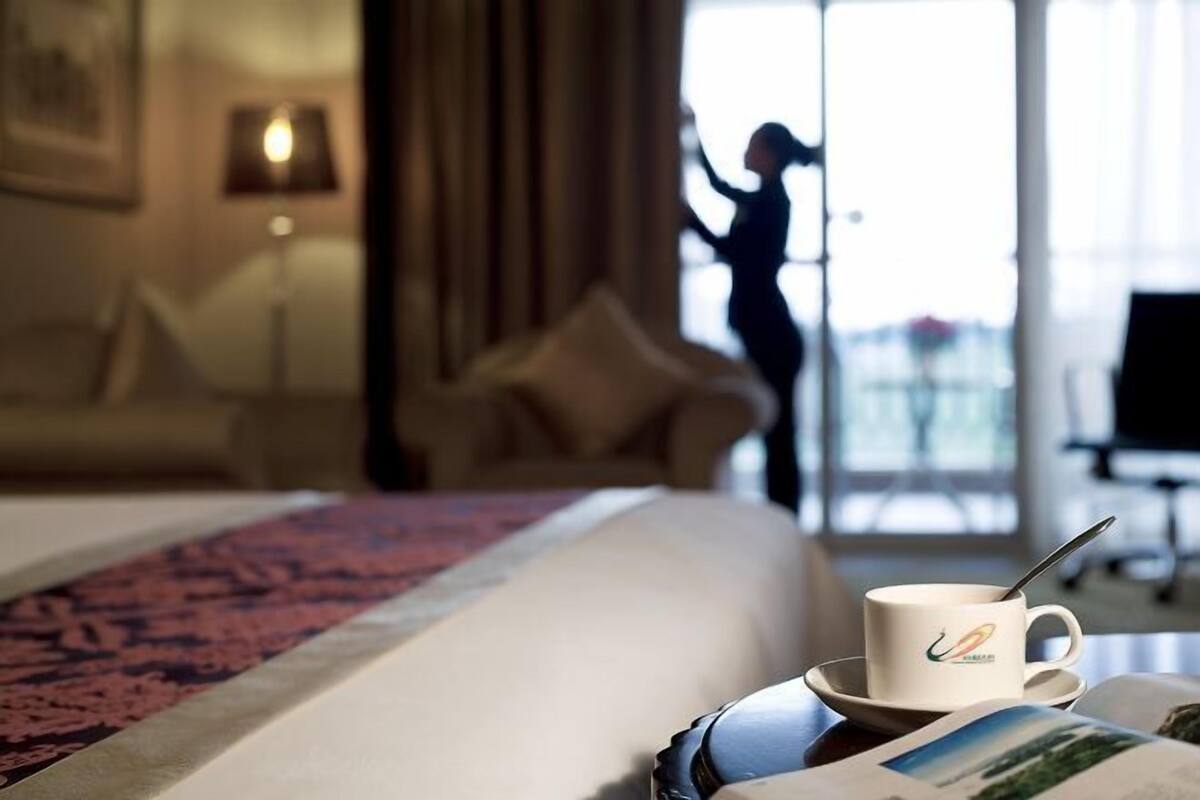 Quarto de hotel com uma cama, uma xícara de café e a vista de alguém do lado de fora.